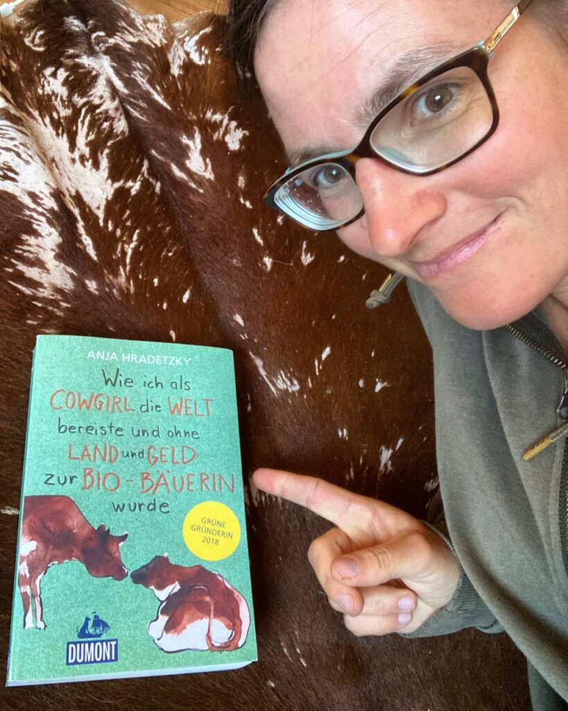 Anja Hradetzky zeigt auf ihr Buch ‚Wie ich als Cowgirl die Welt bereiste und ohne Land und Geld zur Bio-Bäuerin wurde‘ 